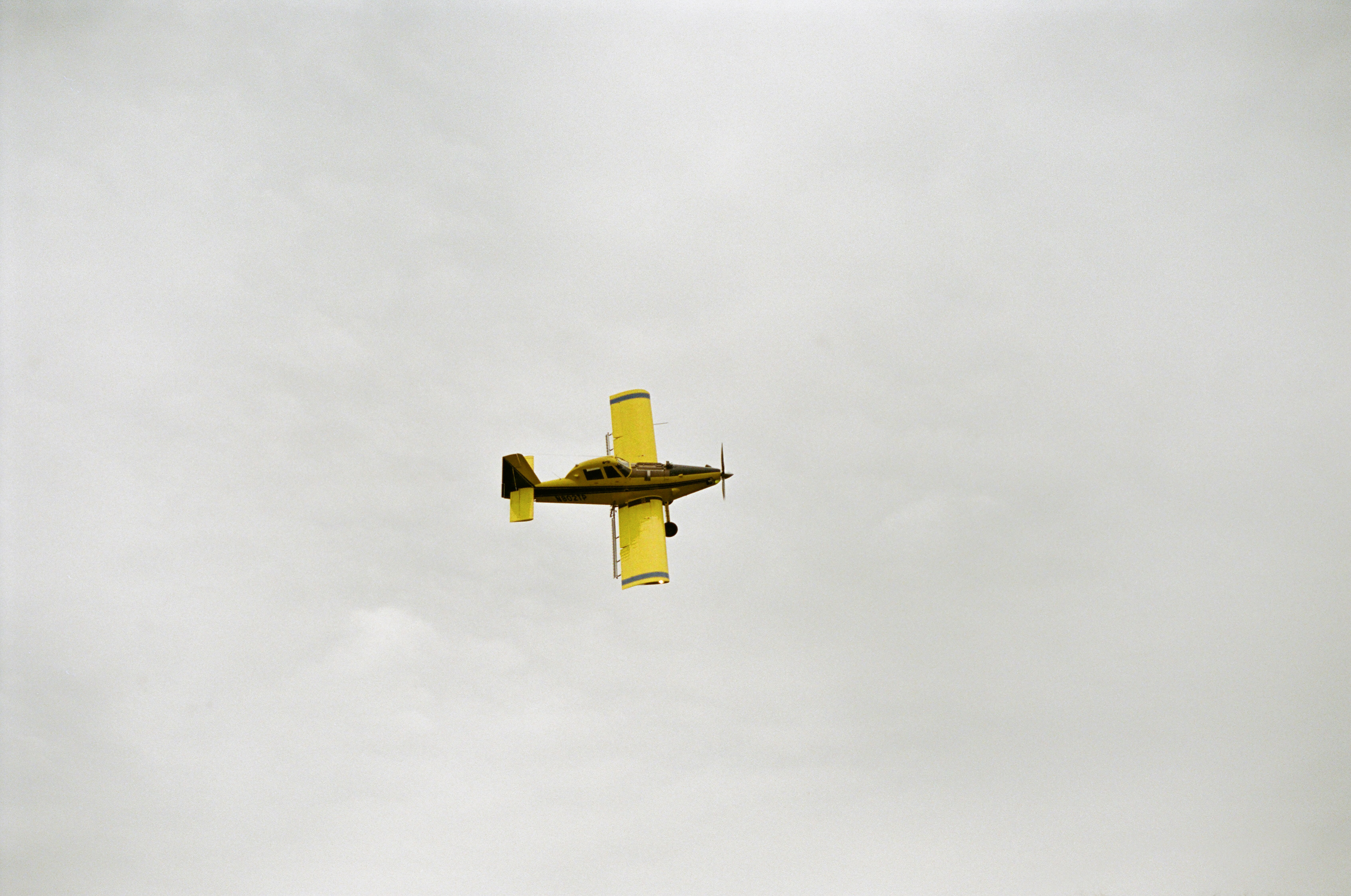 yellow bi-plane flying under white clouds